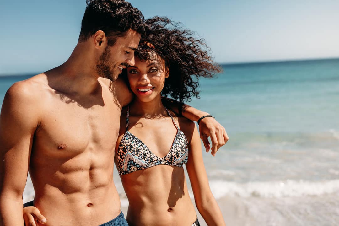 Man and woman on beach in swimsuits with bodies made ideal through plastic surgery, acting as examples of why someone would leave a cosmetic surgery testimonial.